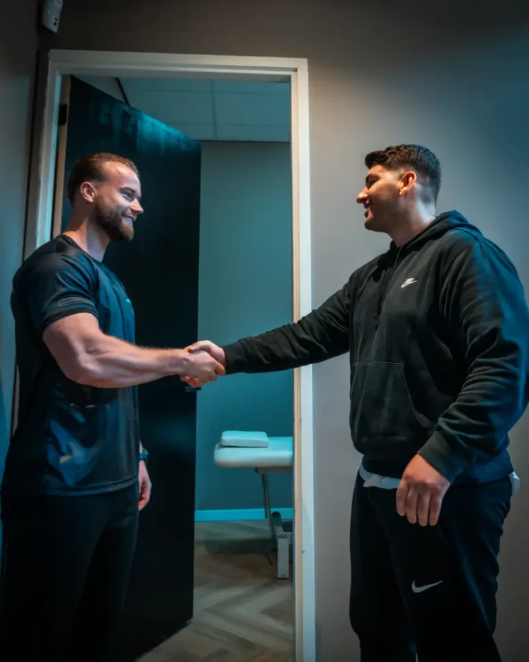 Fysiotherapeut biedt persoonlijke begeleiding tijdens een functionele trainingsoefening in de gym van Fundamentals Alkmaar.