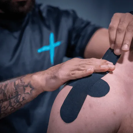 Fysiotherapeut brengt kinesiotape aan op schouder van patiënt