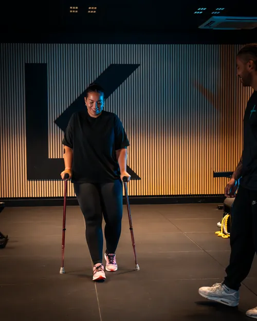 Vrouw loopt glimlachend met nordic walking stokken, ondersteund door fysiotherapeut bij Fysio & Motion IJburg